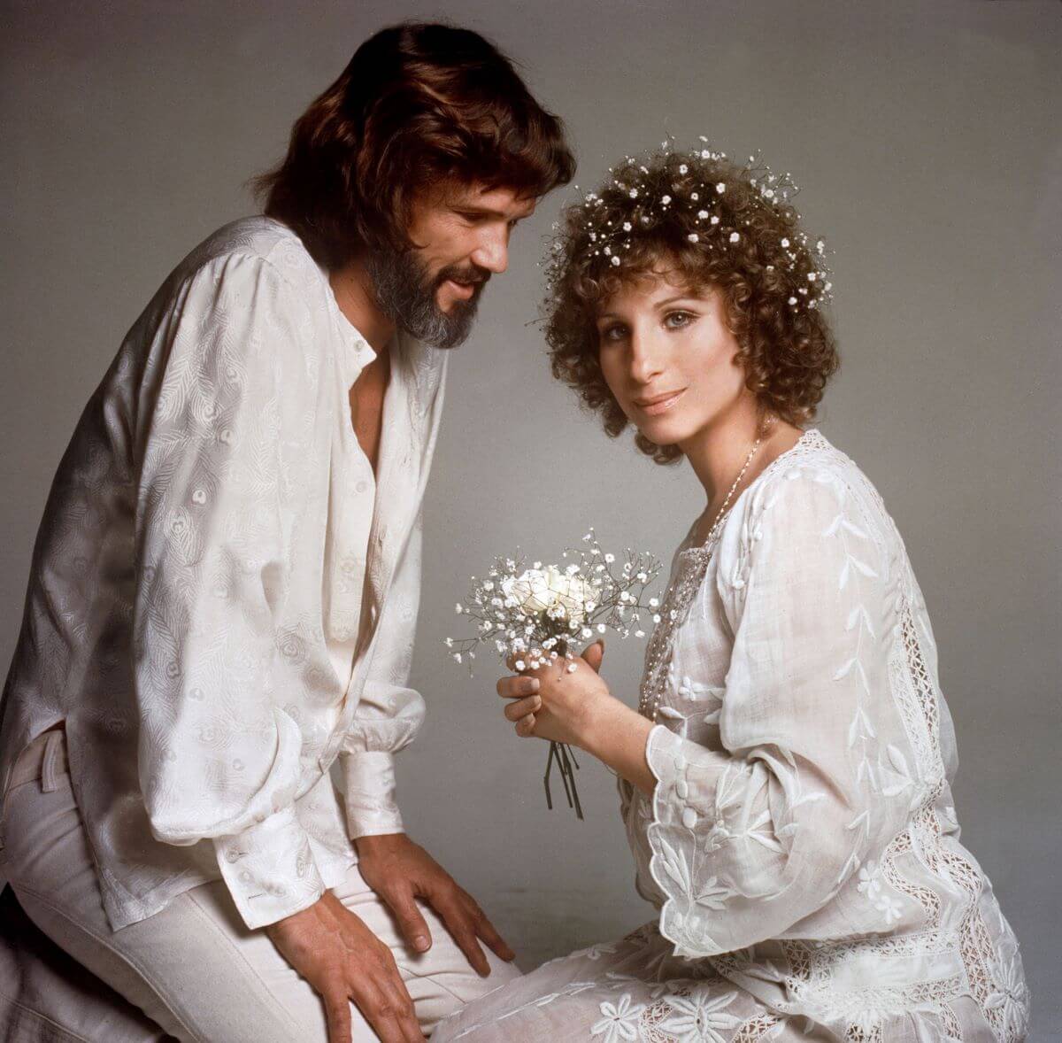 Kris Kristofferson and Barbra Streisand wear white on the set of 'A Star Is Born.' Streisand holds white flowers and has flowers in her hair.