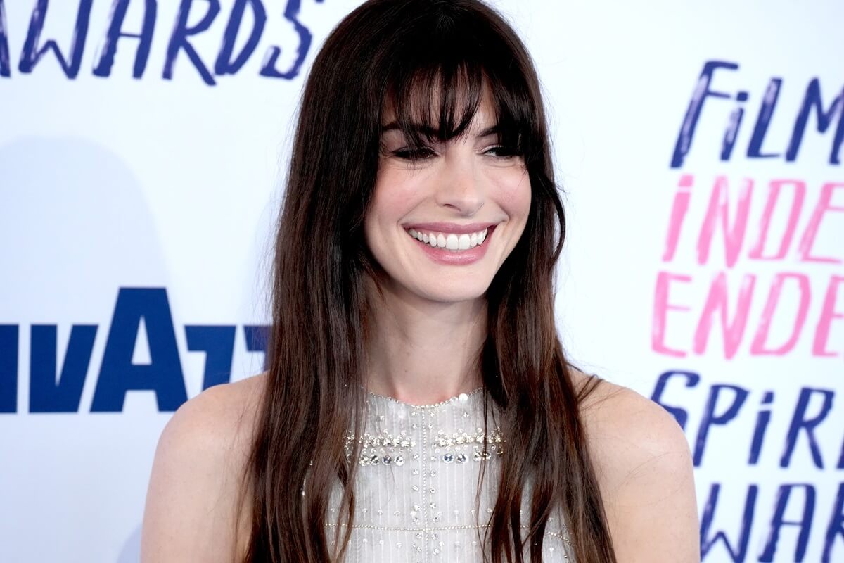 Anne Hathaway smiling the 2024 Film Independent Spirit Awards in a white dress.