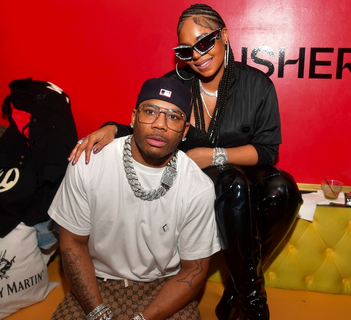 Couple Nelly and Ashanti sit together on a yellow couch at Usher's "Coming Home" Album Release party