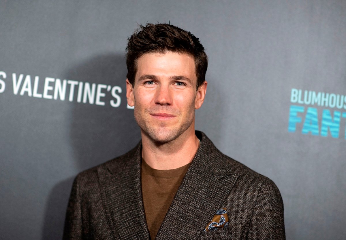 Austin Stowell wears a brown suit and smiles for cameras at the premiere of 'Fantasy Island'