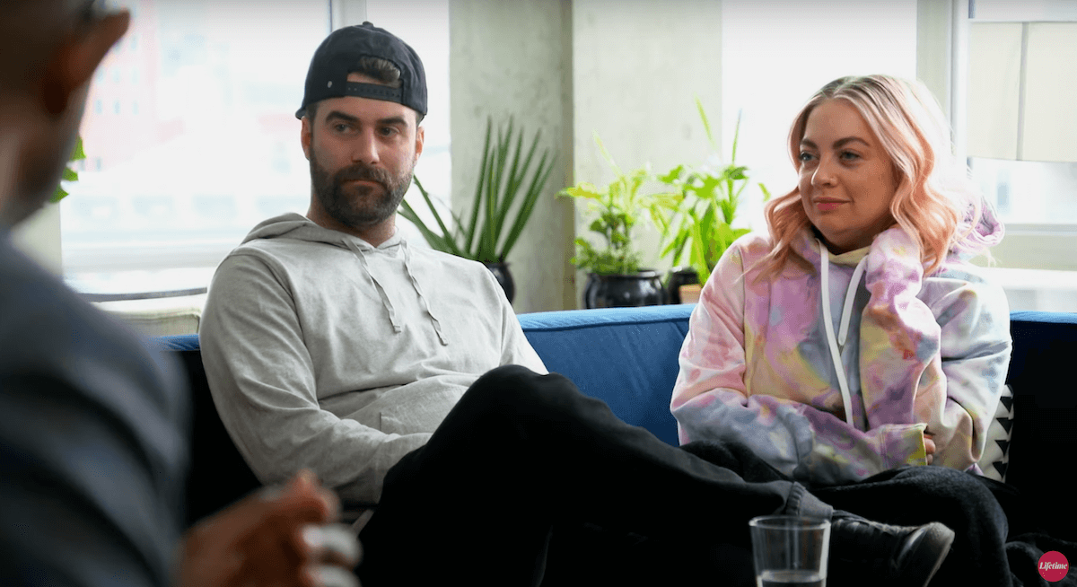 Austin, wearing a backwards baseball cap, sitting next to Becca on a couch