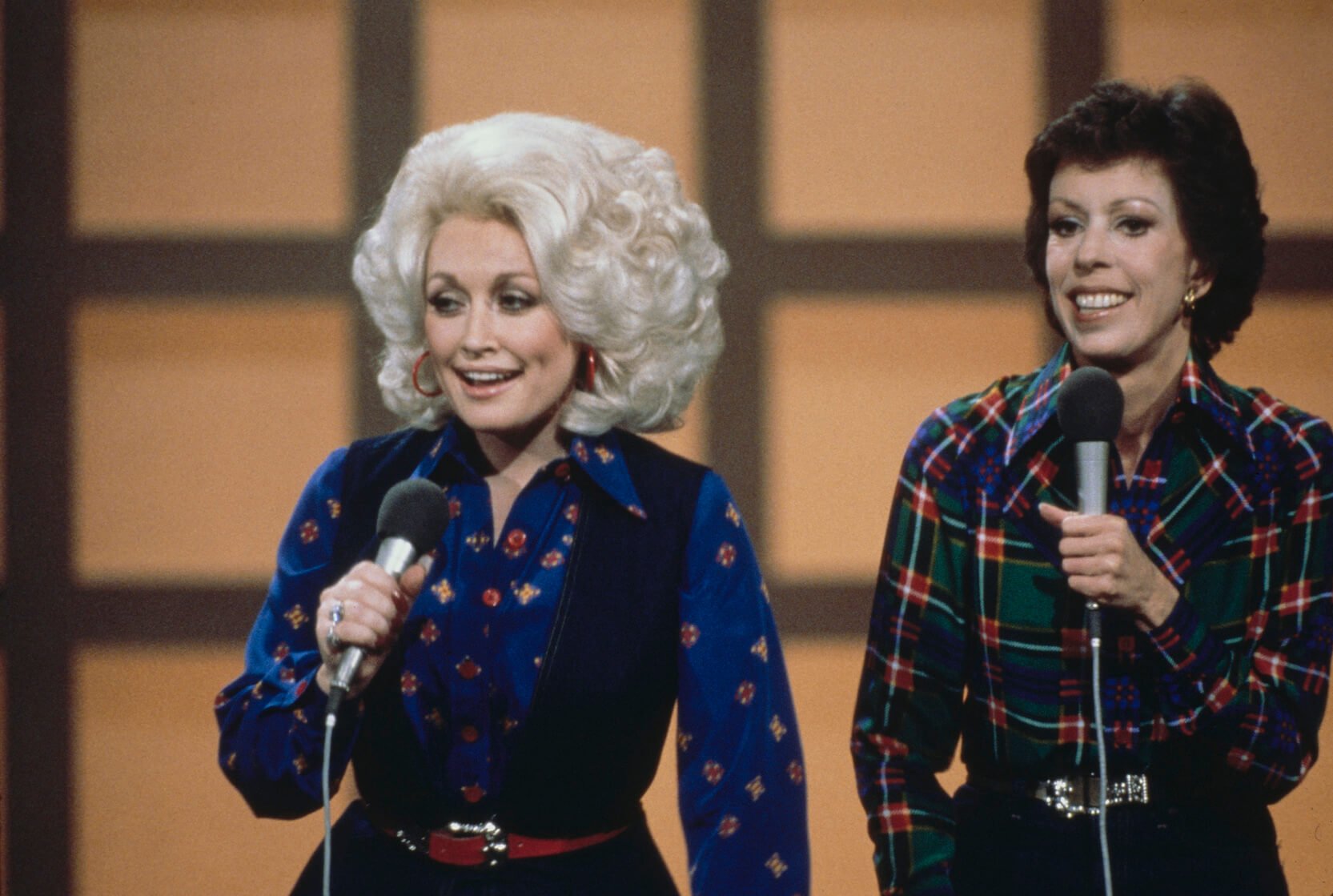 Dolly Parton holding a microphone and standing in front of Carol Burnett