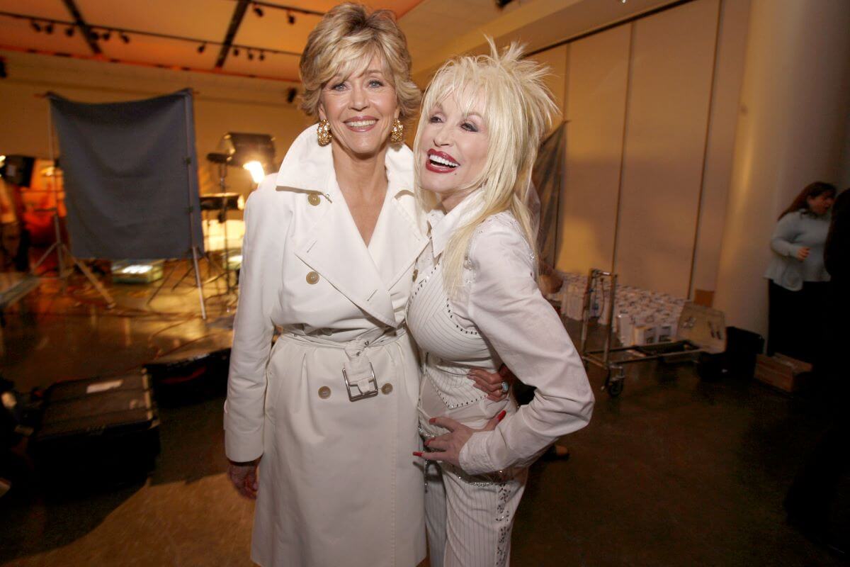 Dolly Parton and Jane Fonda wear white and embrace.