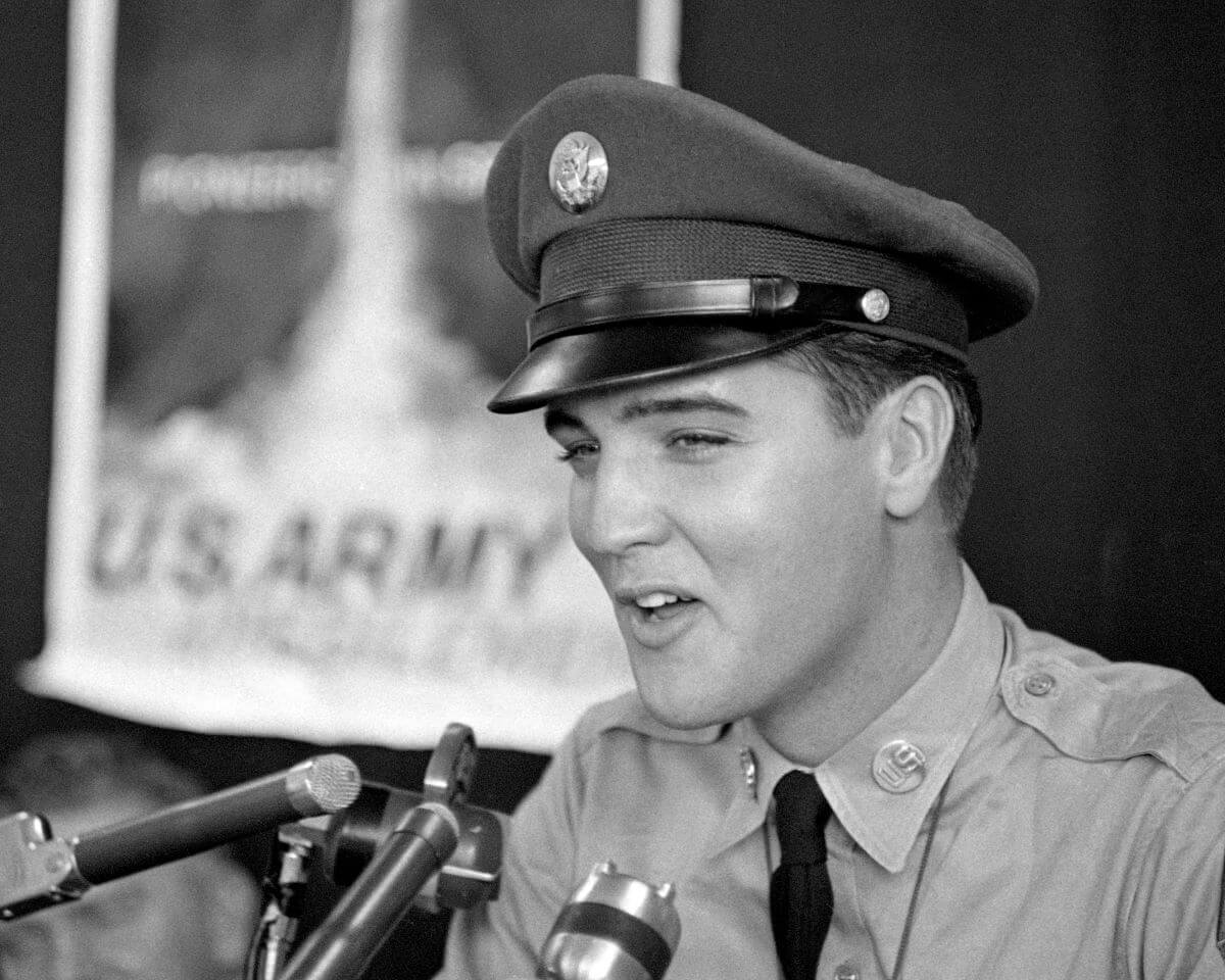 A black and white picture of Elvis in his military uniform and talking into multiple microphones before leaving for Germany.