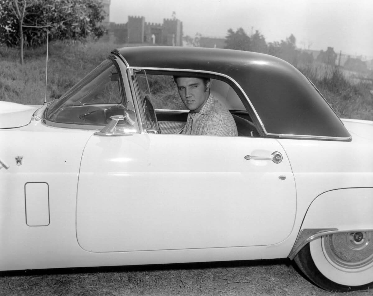 A black and white picture of Elvis sitting in a car and looking out the window.