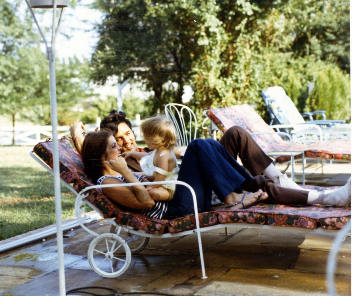 Priscilla and Elvis Presley lay in lawn chairs. Lisa Marie Presley sits on Priscilla's stomach.
