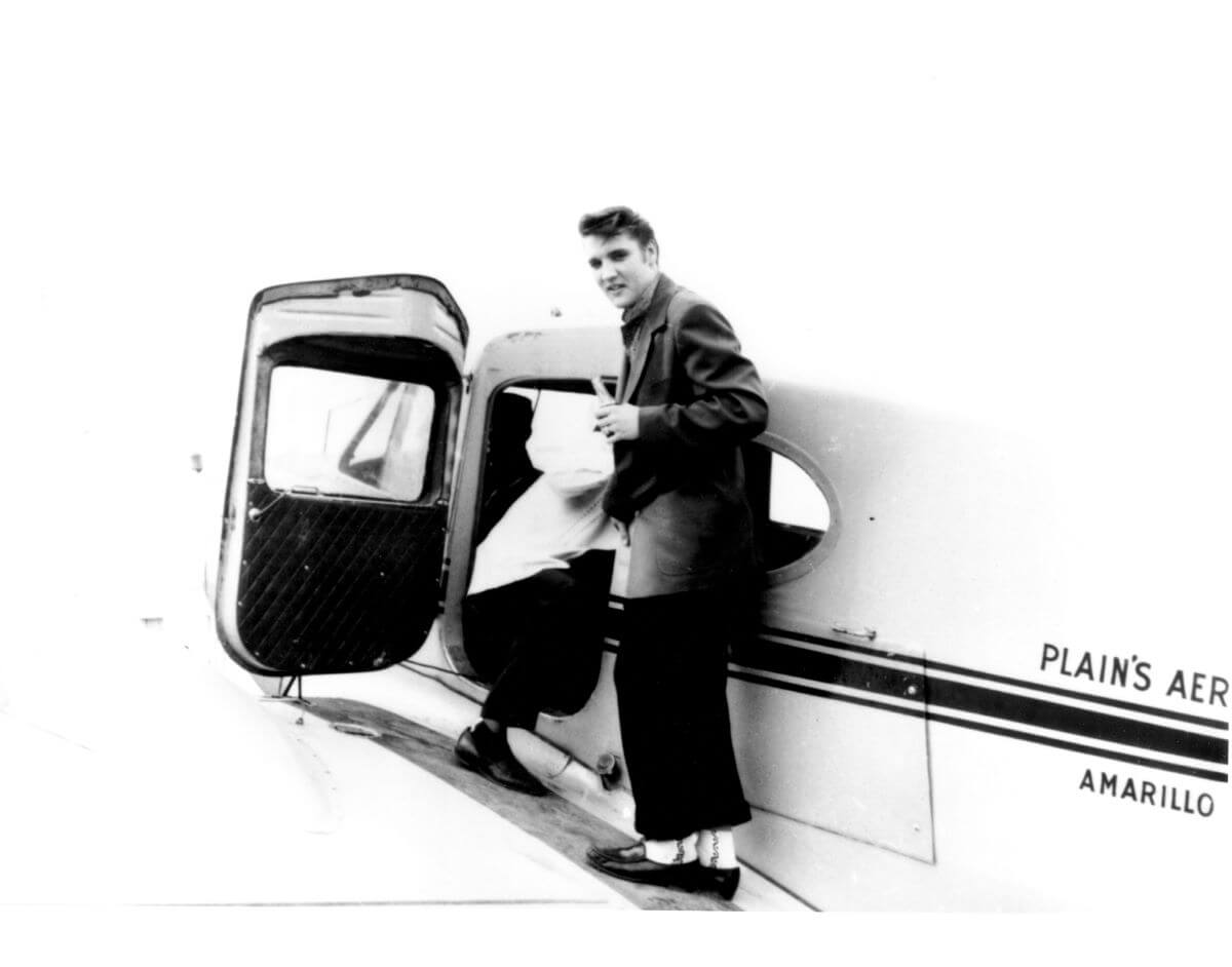 A black and white picture of Elvis about to board a small airplane.