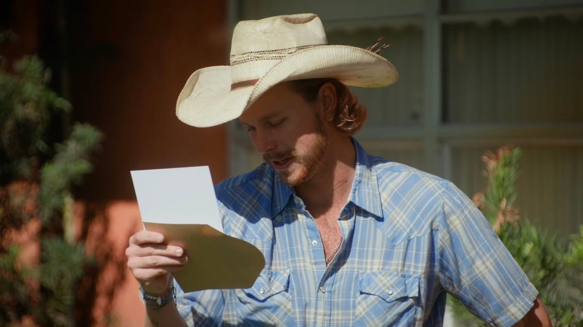 Farmer Nathan, wearing a cowboy hat, reading a note in 'Farmer Wants a Wife' Season 2