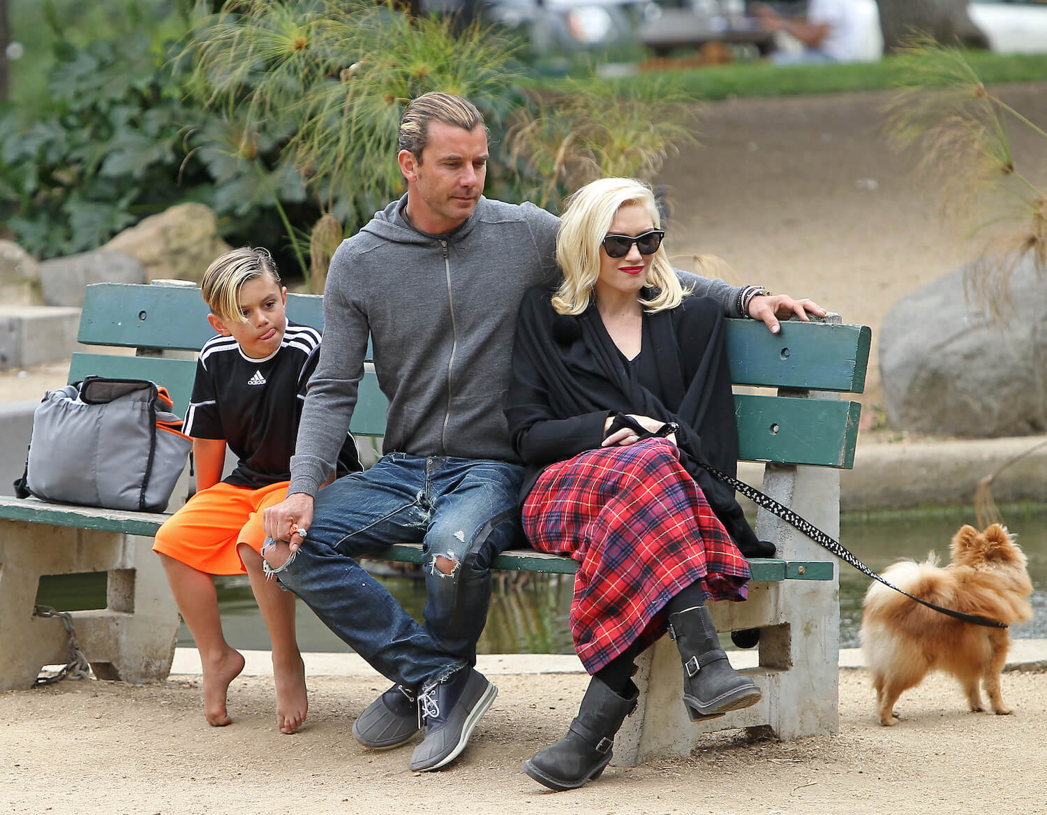 Gavin Rossdale and Gwen Stefani sitting next to each other on a bench with their son, Kingston