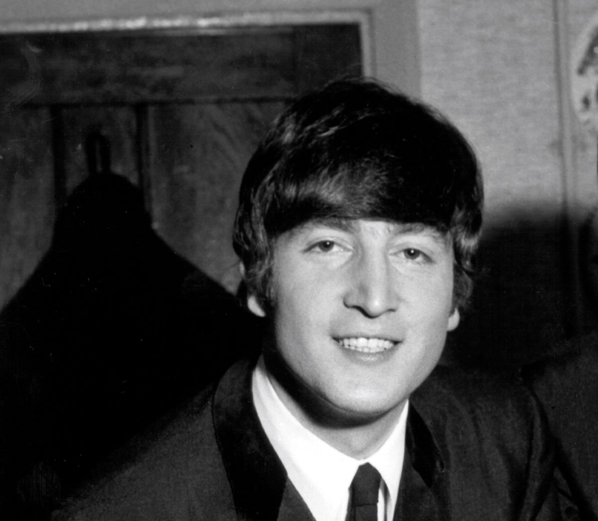 A black and white picture of John Lennon wearing a suit and smiling.