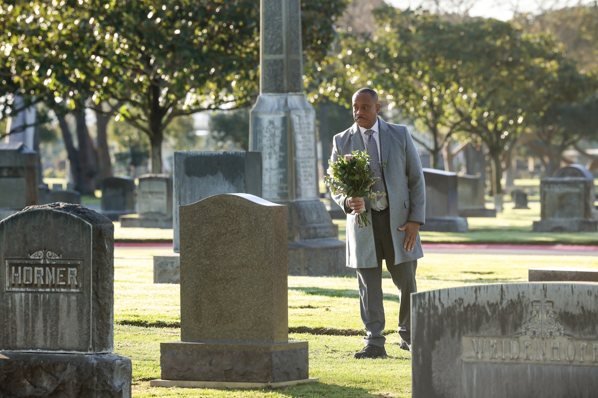 Man standing with flowers in front of a headstone in 'NCIS' Season 21 Episode 7