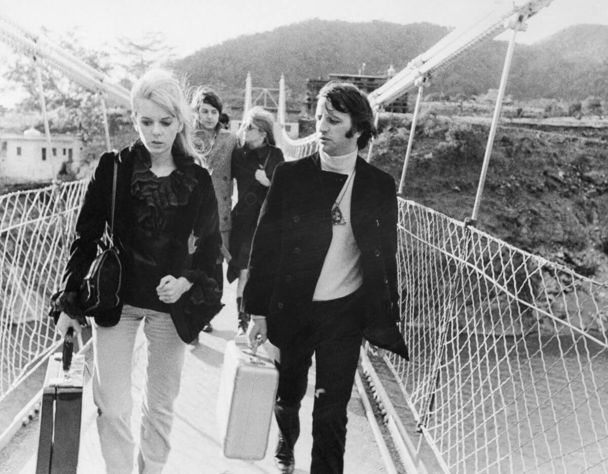 A black and white picture of Ringo Starr and Maureen Starkey crossing a bridge holding suitcases. Paul McCartney and Jane Asher walk behind them.
