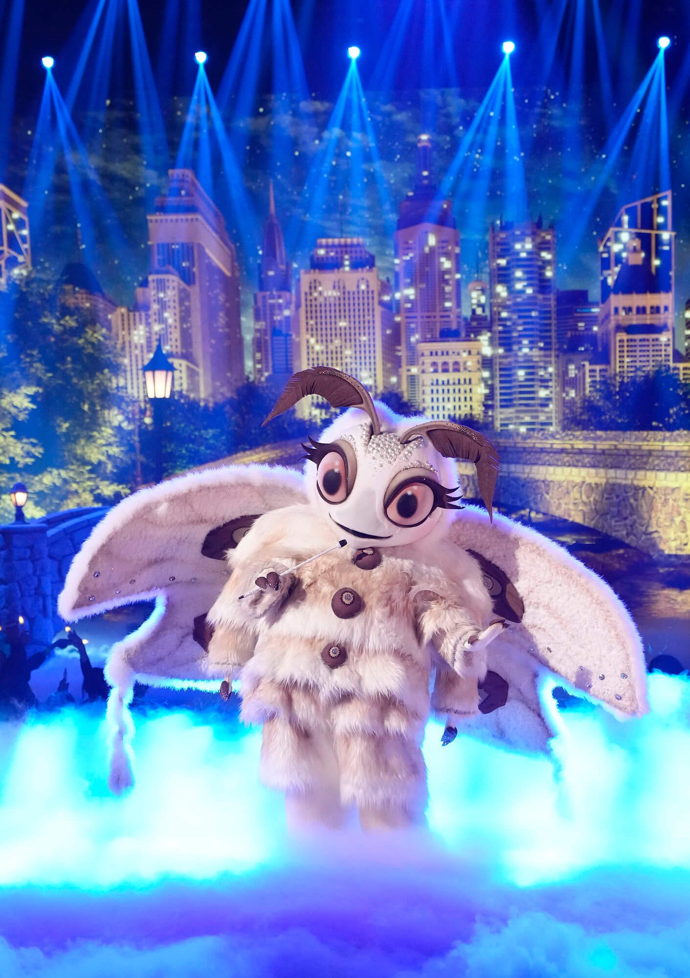 'The Masked Singer' Season 11 Group C singer Poodle Moth on stage illuminated by blue light with a city background 