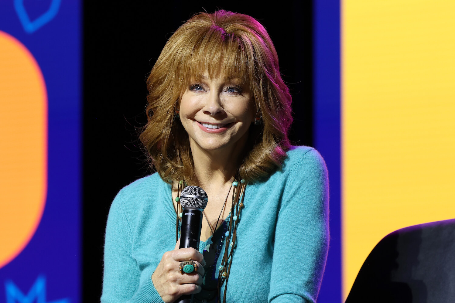 'The Voice' Season 25 coach Reba McEntire smiling while holding a microphone