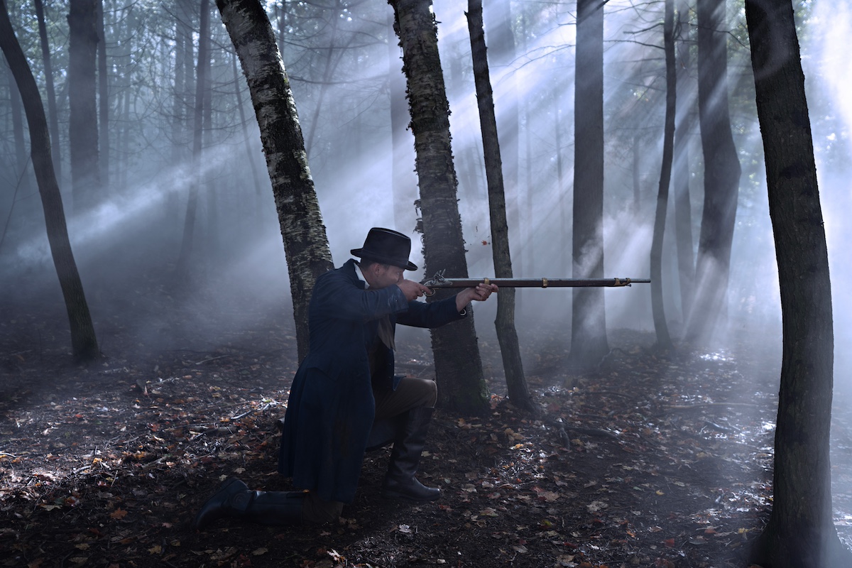 A man in 19th century clothing crouching and holding a rifle in 'The Way Home'