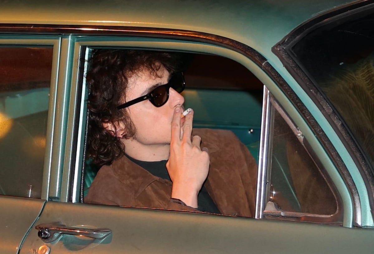 Timothee Chalamet as Bob Dylan, wearing sunglasses and smoking in a car while filming 'A Complete Unknown'