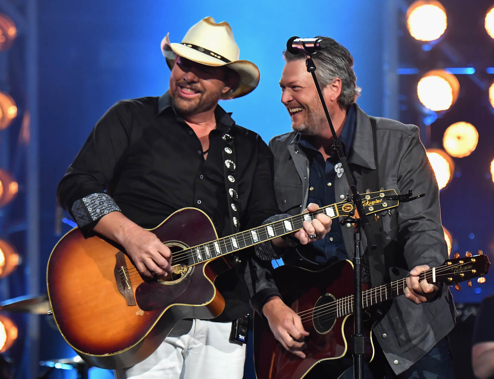 Toby Keith and Blake Shelton laughing on stage while holding guitars