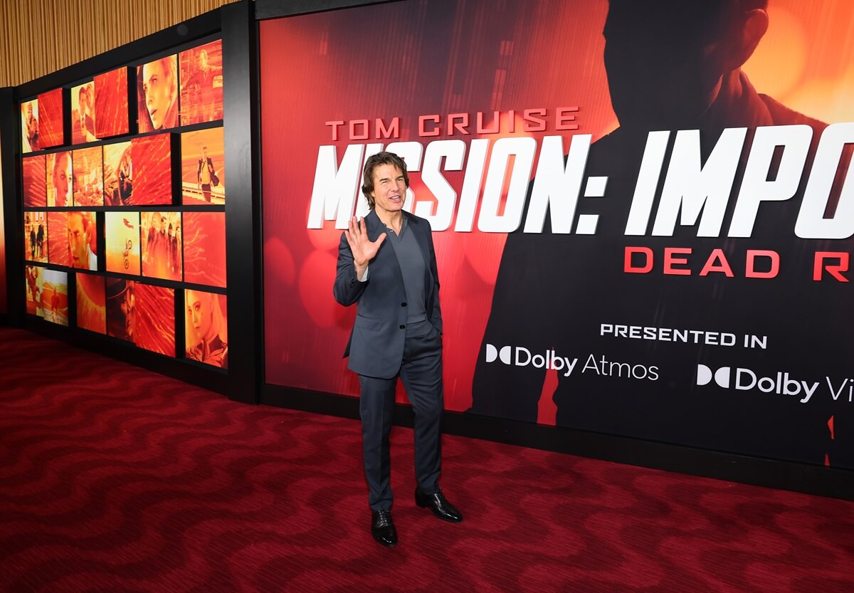 Tom Cruise posing in a black suit in front of a 'Mission Impossible Dead Reckoning Part One' poster.