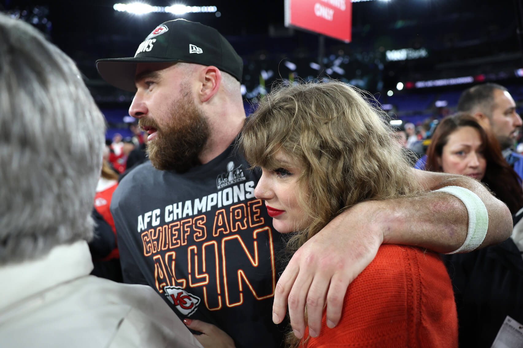 Travis Kelce with his arm around Taylor Swift after a Kansas City Chiefs game. They're surrounded by other people in a crowd.