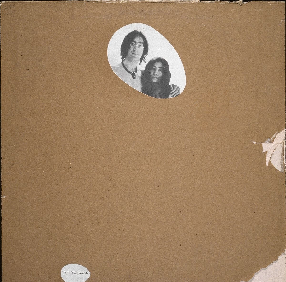 John Lennon and Yoko Ono's face peek out from a circle of the otherwise hidden album cover for 'Two Virgins.' There is brown paper over it.