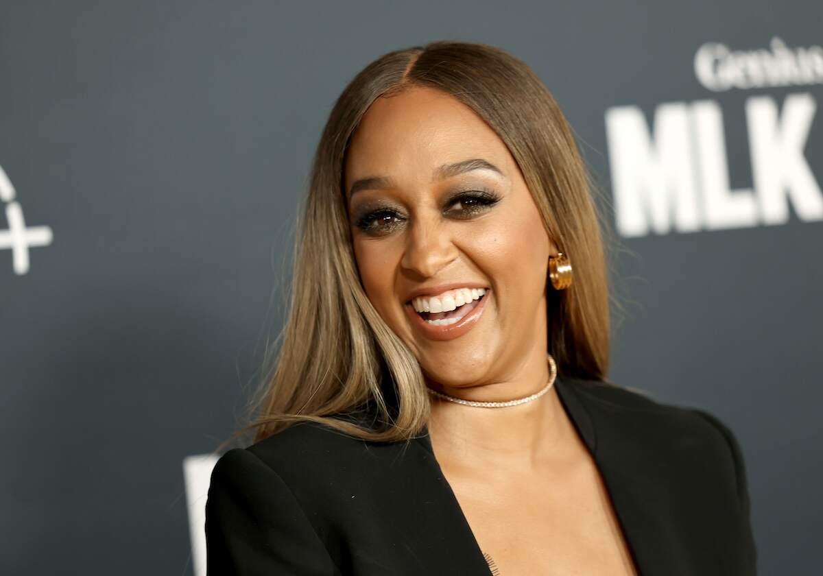 Actor Tia Mowry laughs at a movie premiere wearing a low-cut black blazer and diamond choker necklace