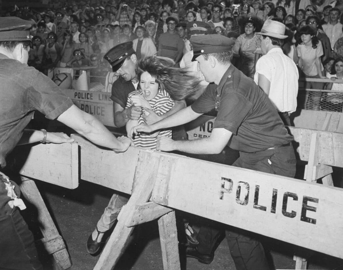 A black and white picture of police officers stopping a Beatles fan who rushes forward.