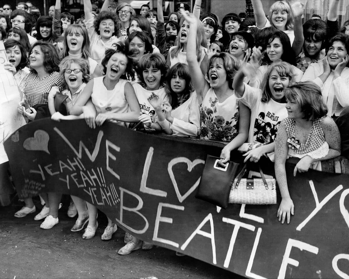 A group of Beatles fans stand behind a banner that says "We Love You Beatles."