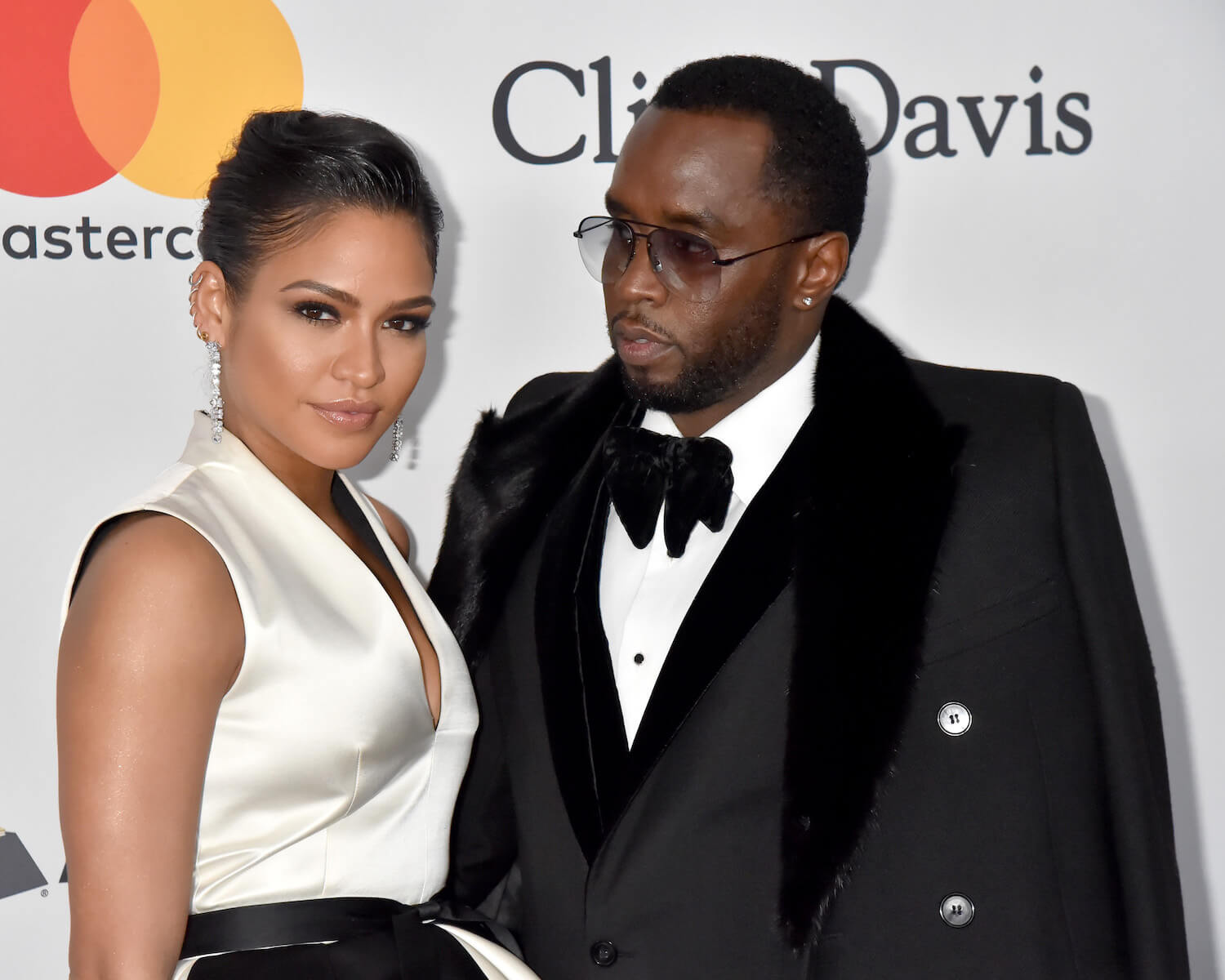 Casandra 'Cassie' Ventura standing next to Sean 'P. Diddy' Combs. Cassie is wearing a white and black dress; Combs is wearing a tuxedo.