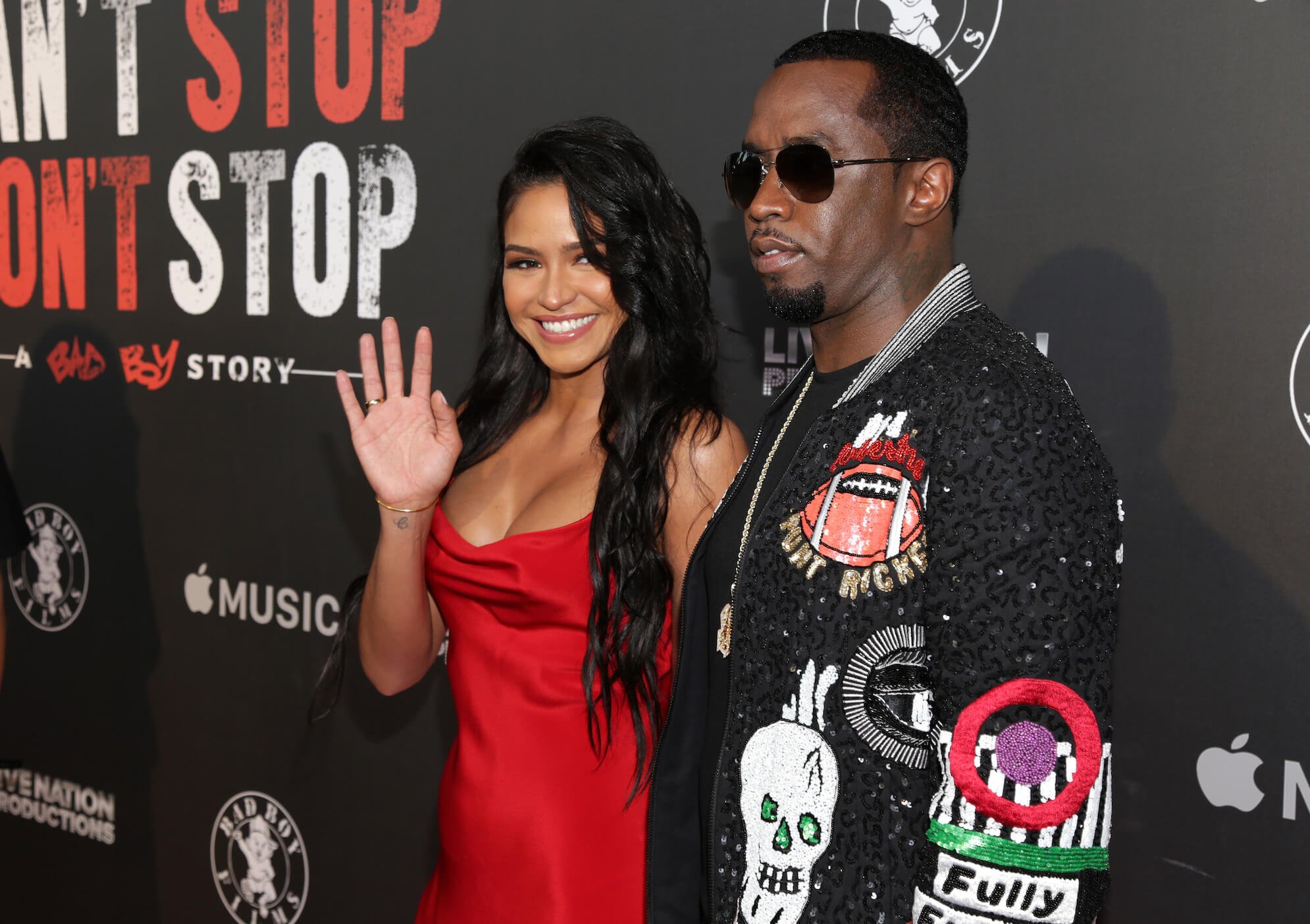 Cassie Ventura waving to cameras and smiling while she holds Sean 'P. Diddy' Combs' hand at an event