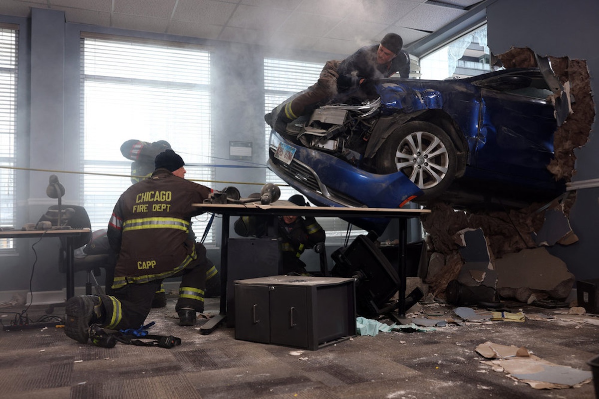 A firefighter crouches in front of a car that's gone through a wall on 'Chicago Fire'