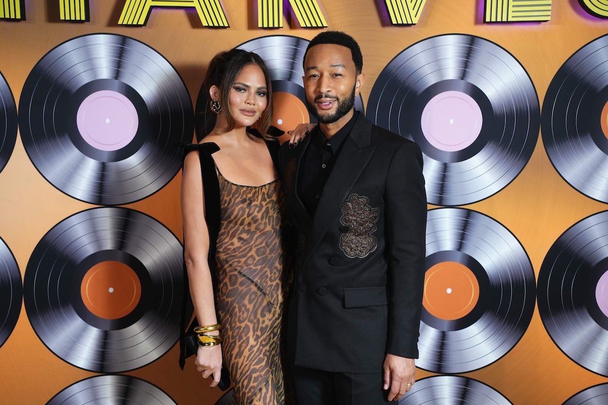 Married couple Chrissy Teigen and John Legend wear formalwear and pose for a photo in front of large records