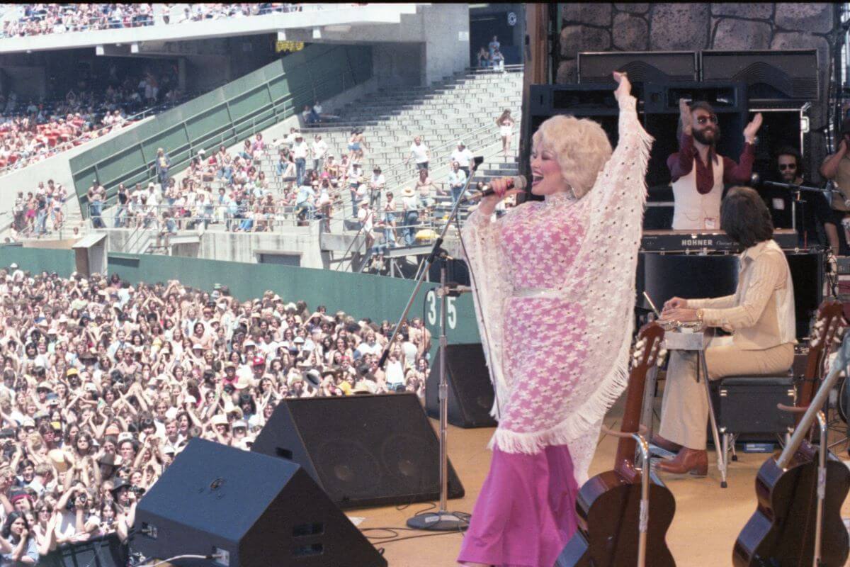Dolly Parton sings into a microphone while onstage in front of a large audience.