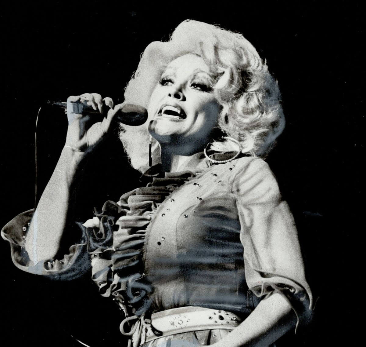 A black and white picture of Dolly Parton singing into a microphone.