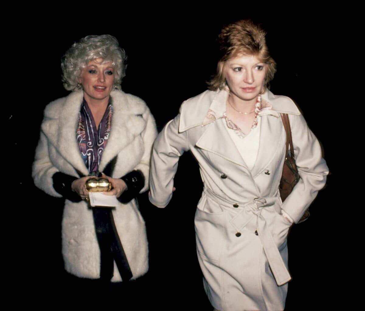 Dolly Parton and her best friend Judy Ogle walk outside together. They both wear coats.