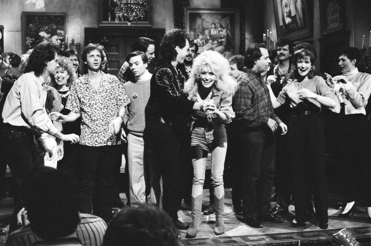 A black and white picture of Dolly Parton on stage with the cast of 'SNL.'