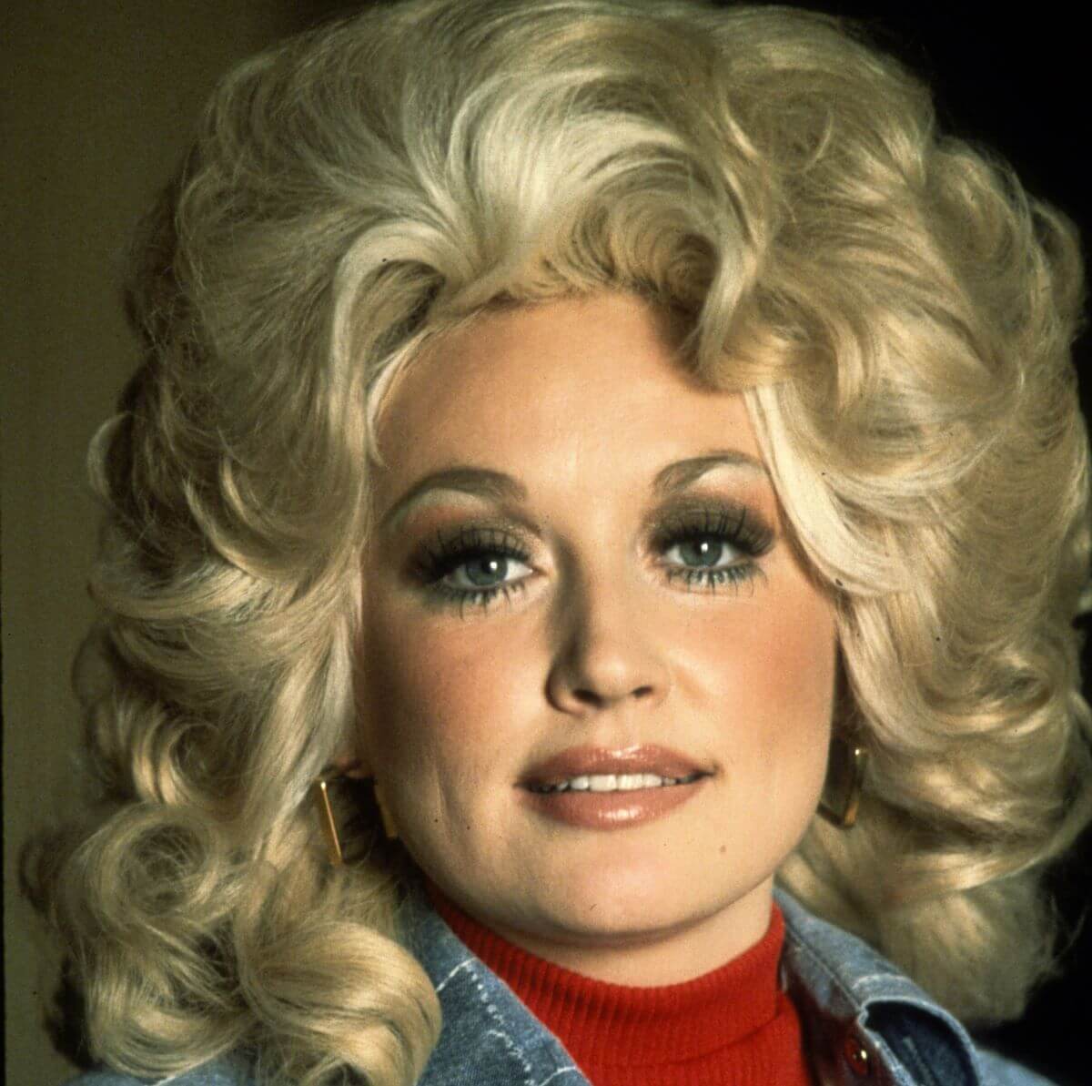 Dolly Parton wears a red shirt and denim jacket.