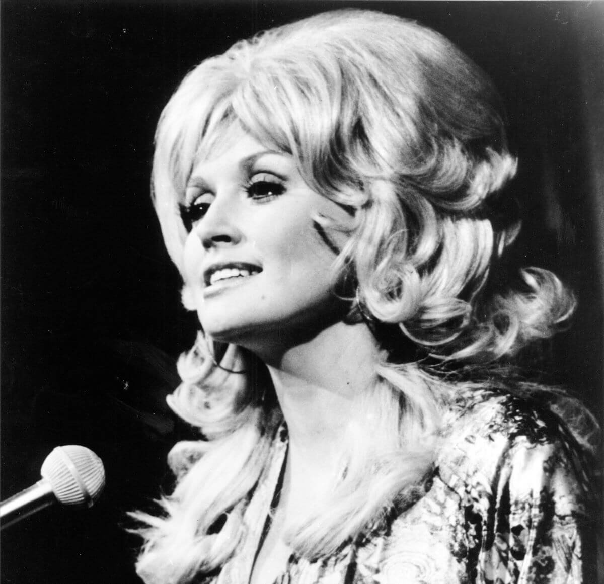 A black and white picture of Dolly Parton standing in front of a microphone.