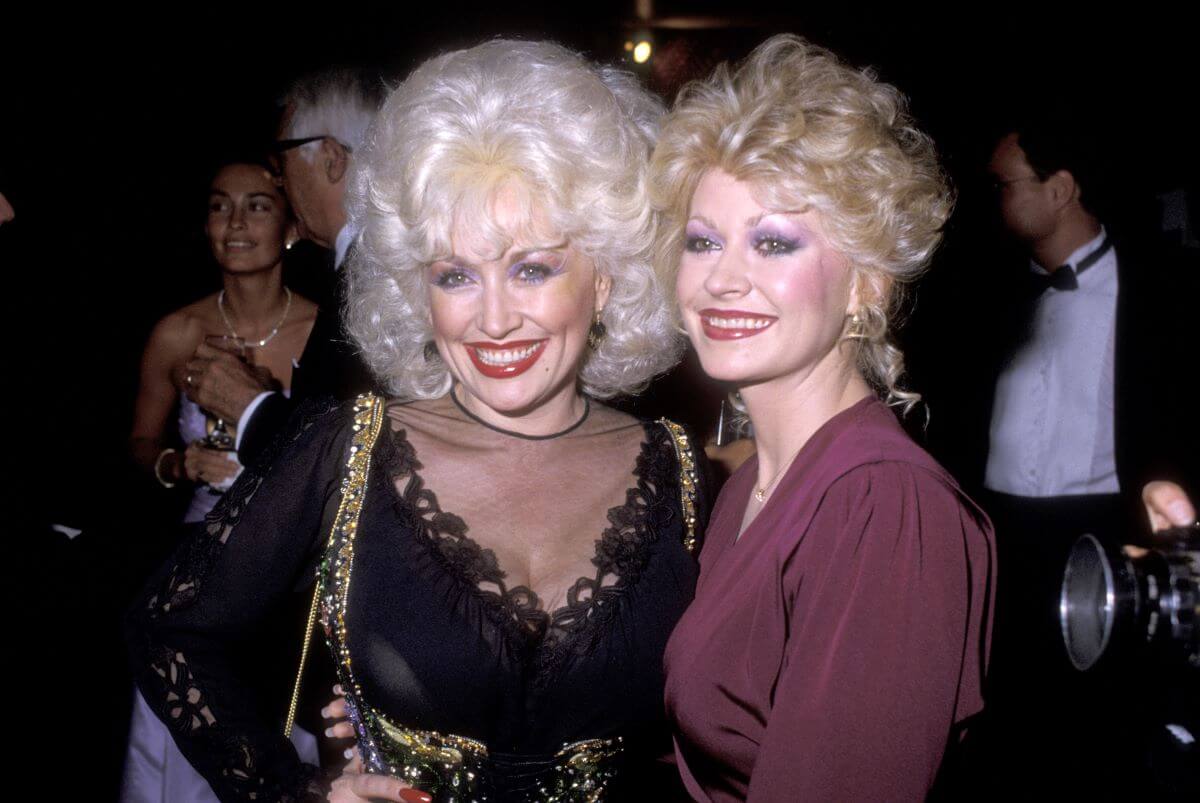 Dolly Parton wears black and stands with her sister Rachel, who wears purple.