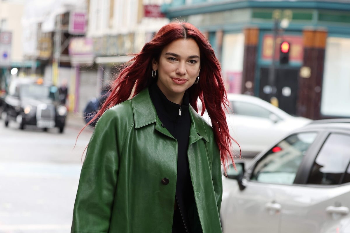 Singer Dua Lipa wears a green trench coat while walking a London street