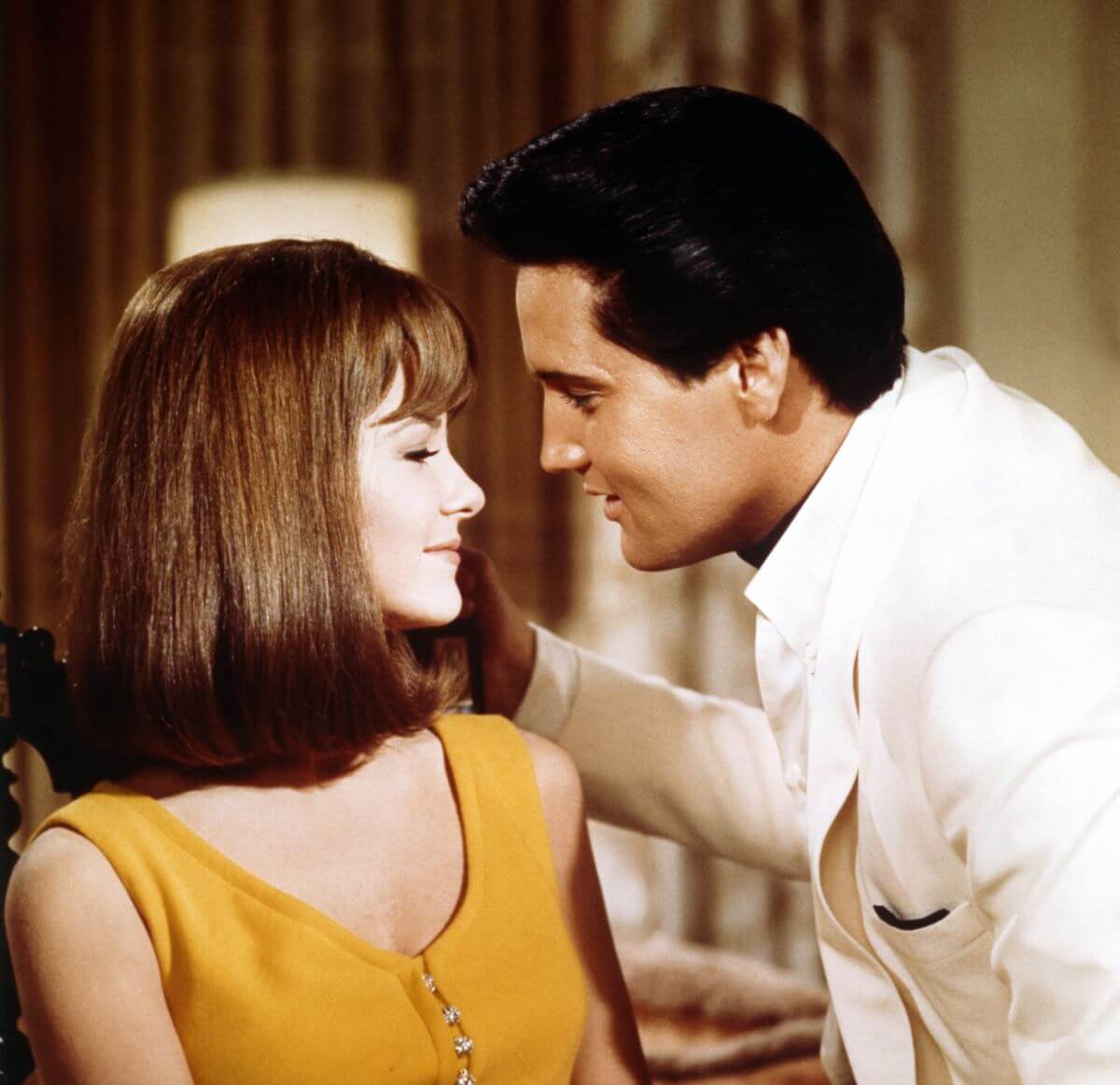 Elvis leans in toward Shelley Fabares. He wears a white shirt and she wears a yellow tank top.