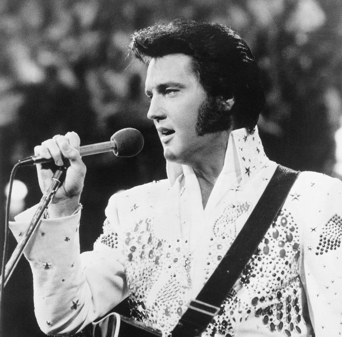 A black and white picture of Elvis Presley holding a microphone up to his face.