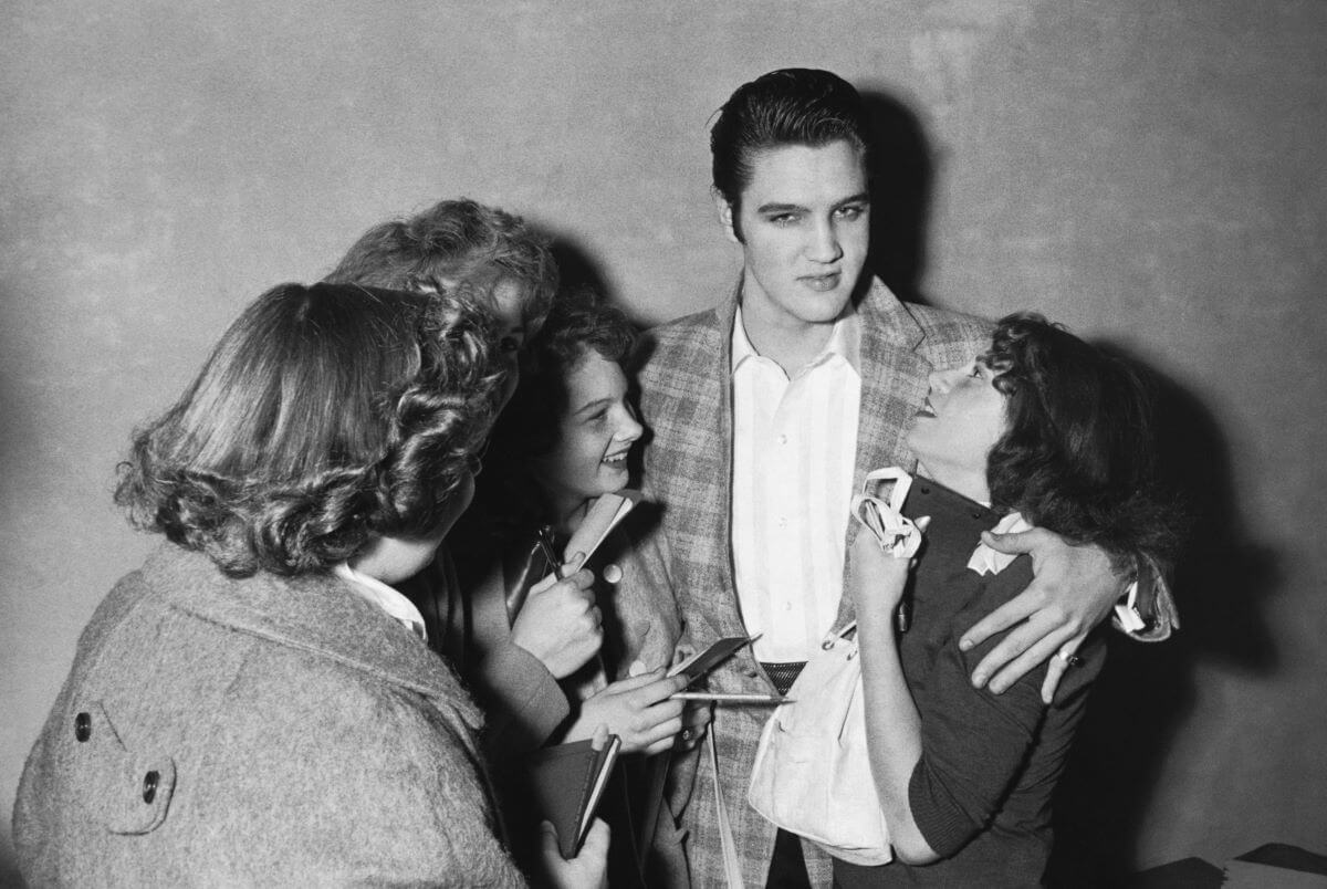 A black and white picture of Elvis standing with a group of female fans.
