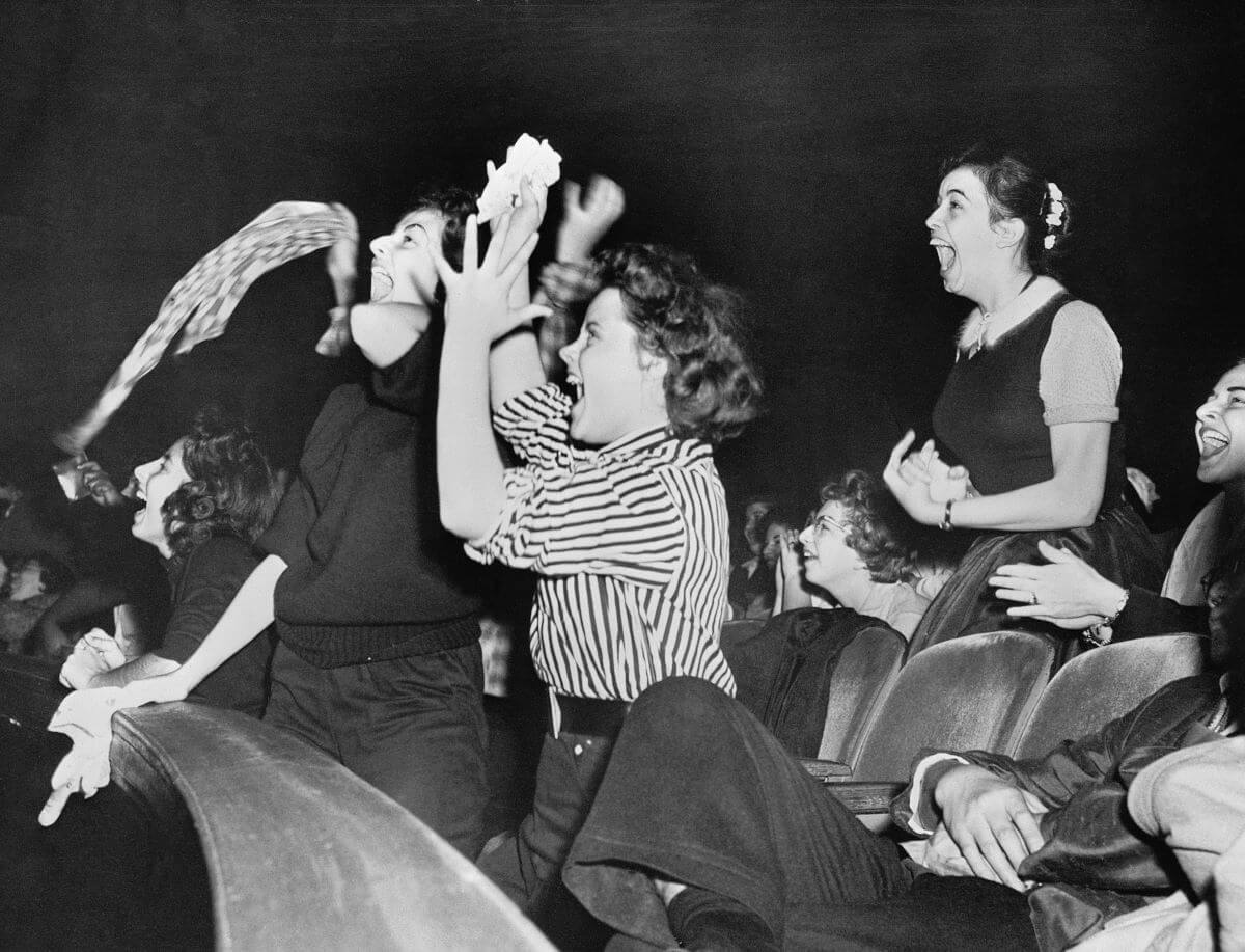 A black and white picture of Elvis fans screaming and jumping up.