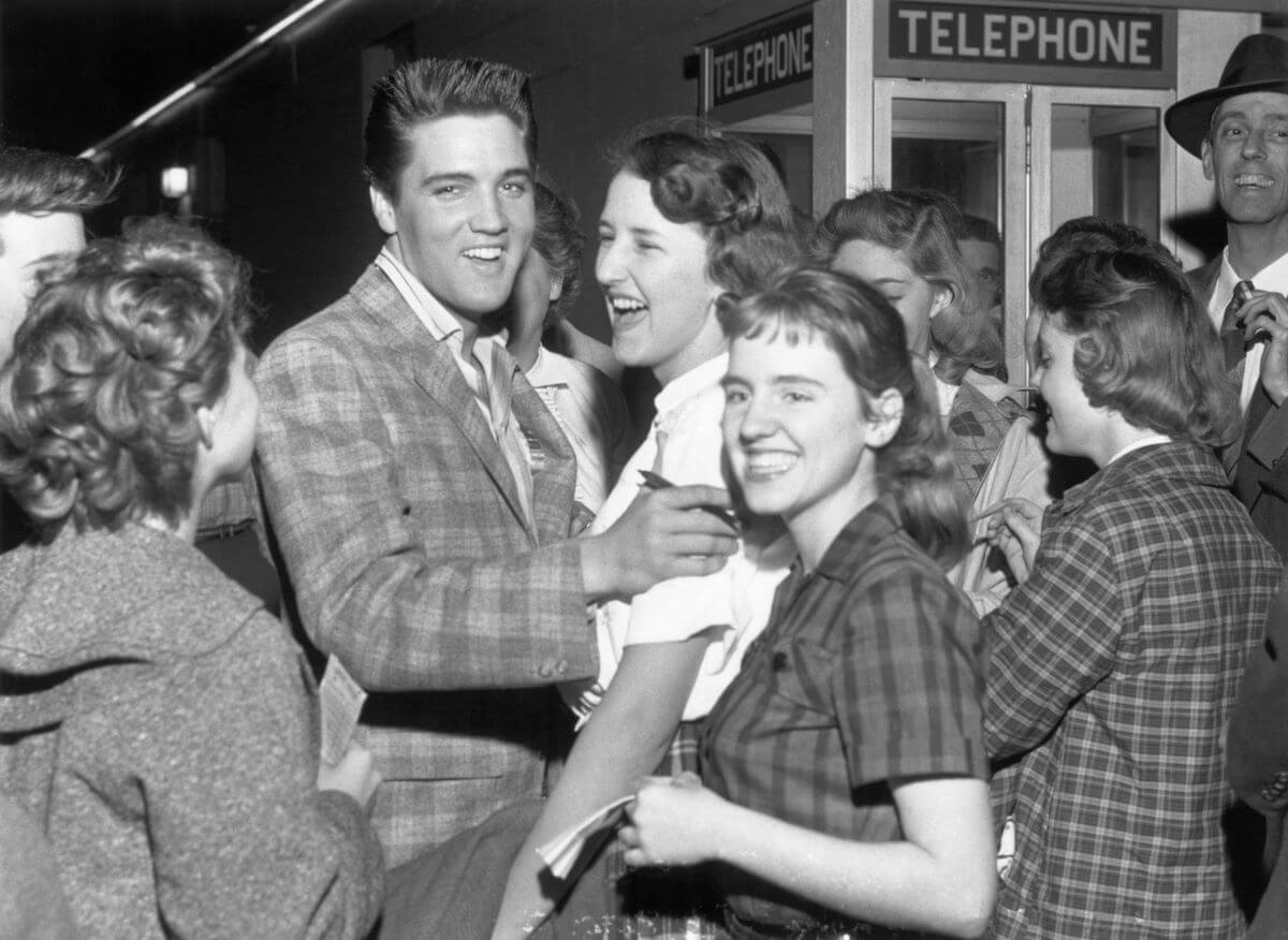 A black and white picture of Elvis Presley standing in a crowd of women.