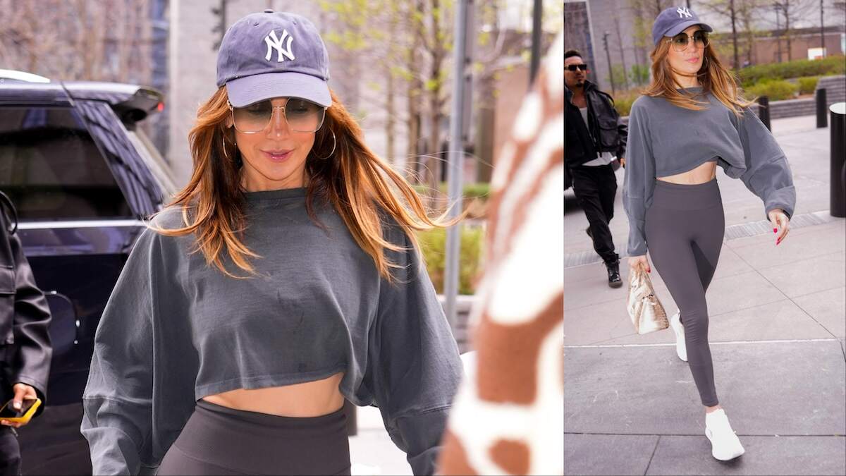 Singer Jennifer Lopez walks across an NYC street in gray leggins and a gray cropped tee shirt, showing her abs