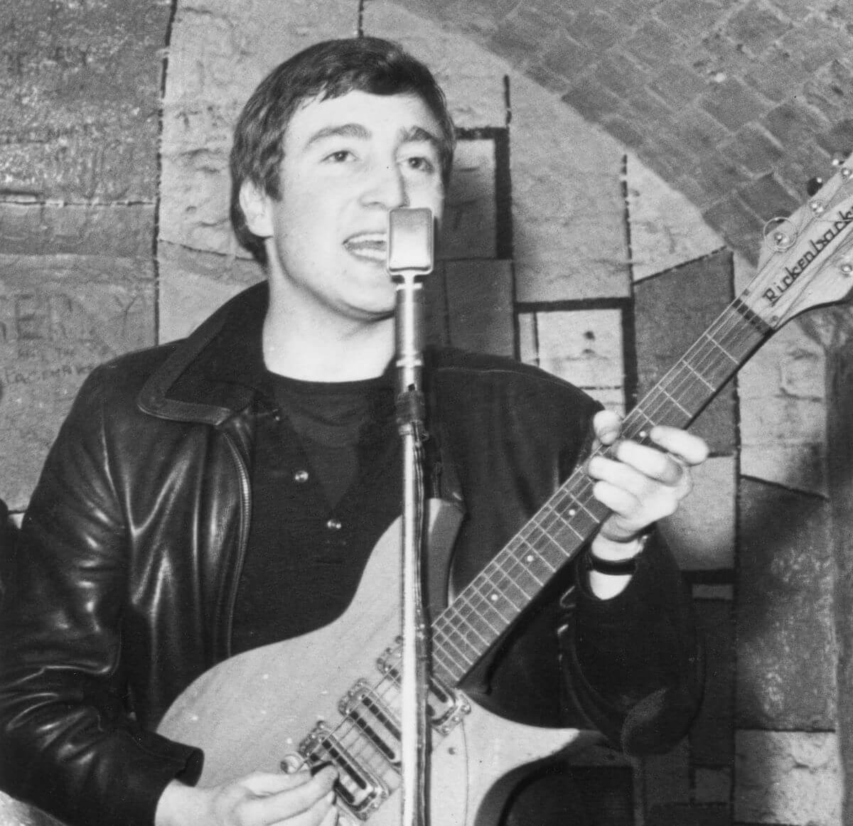 A black and white picture of The Beatles' John Lennon playing guitar and singing into a microphone.