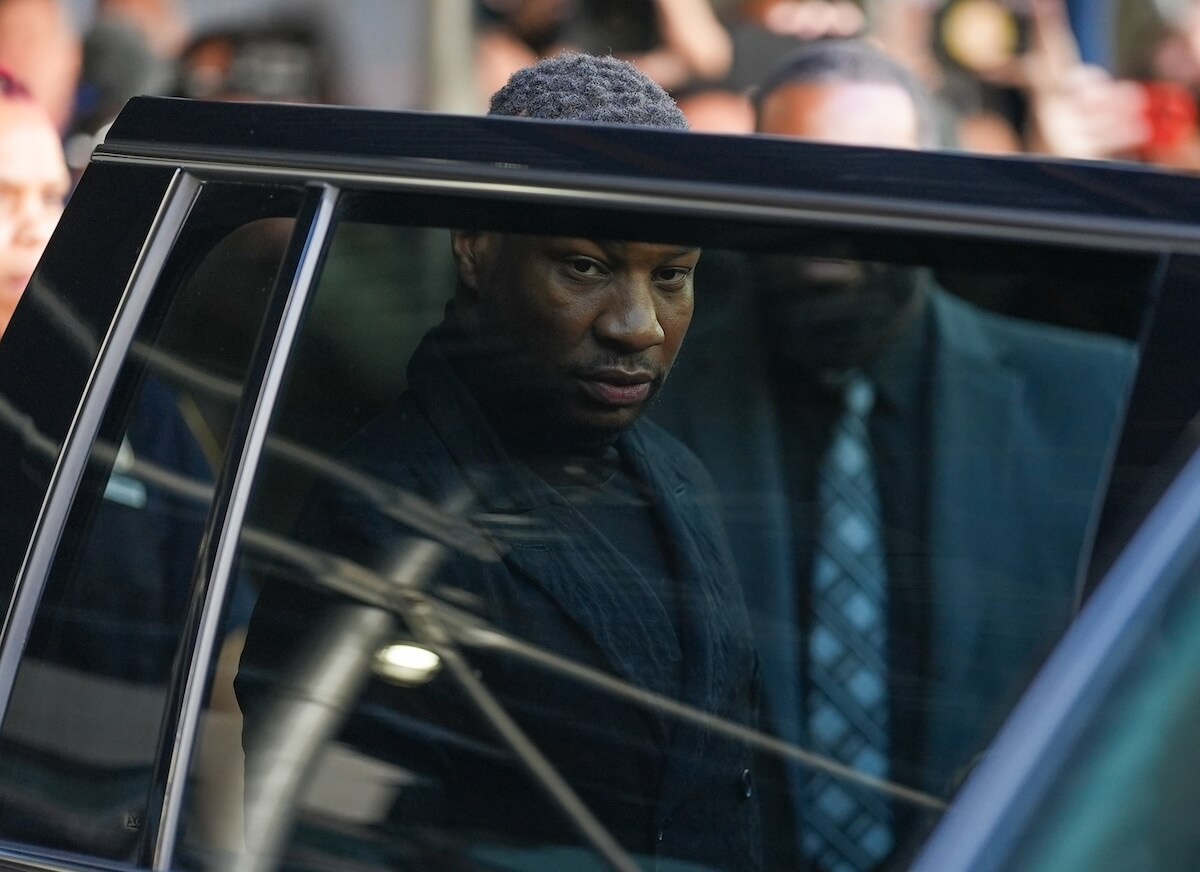 Jonathan Majors seen through the window of an open car door