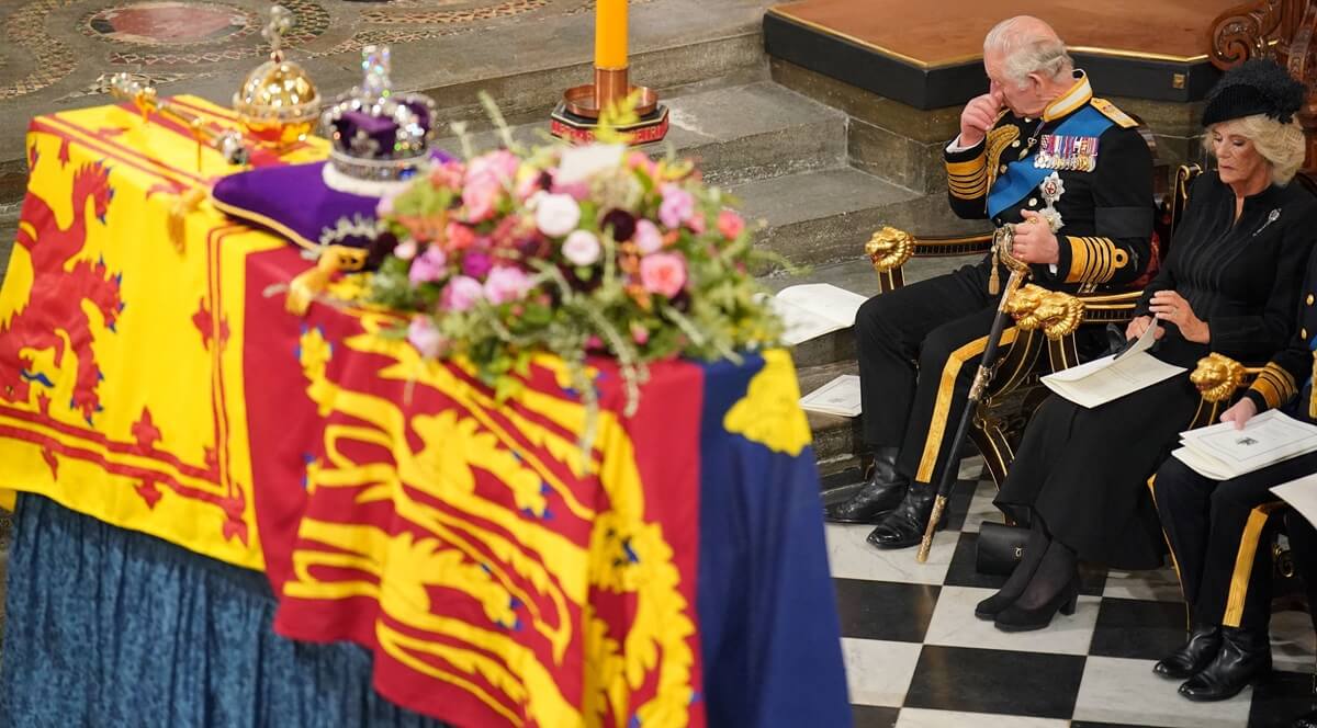 King Charles III sitting in front next to his wife, Camilla, wiping his eyes during Queen Elizabeth II's state funeral