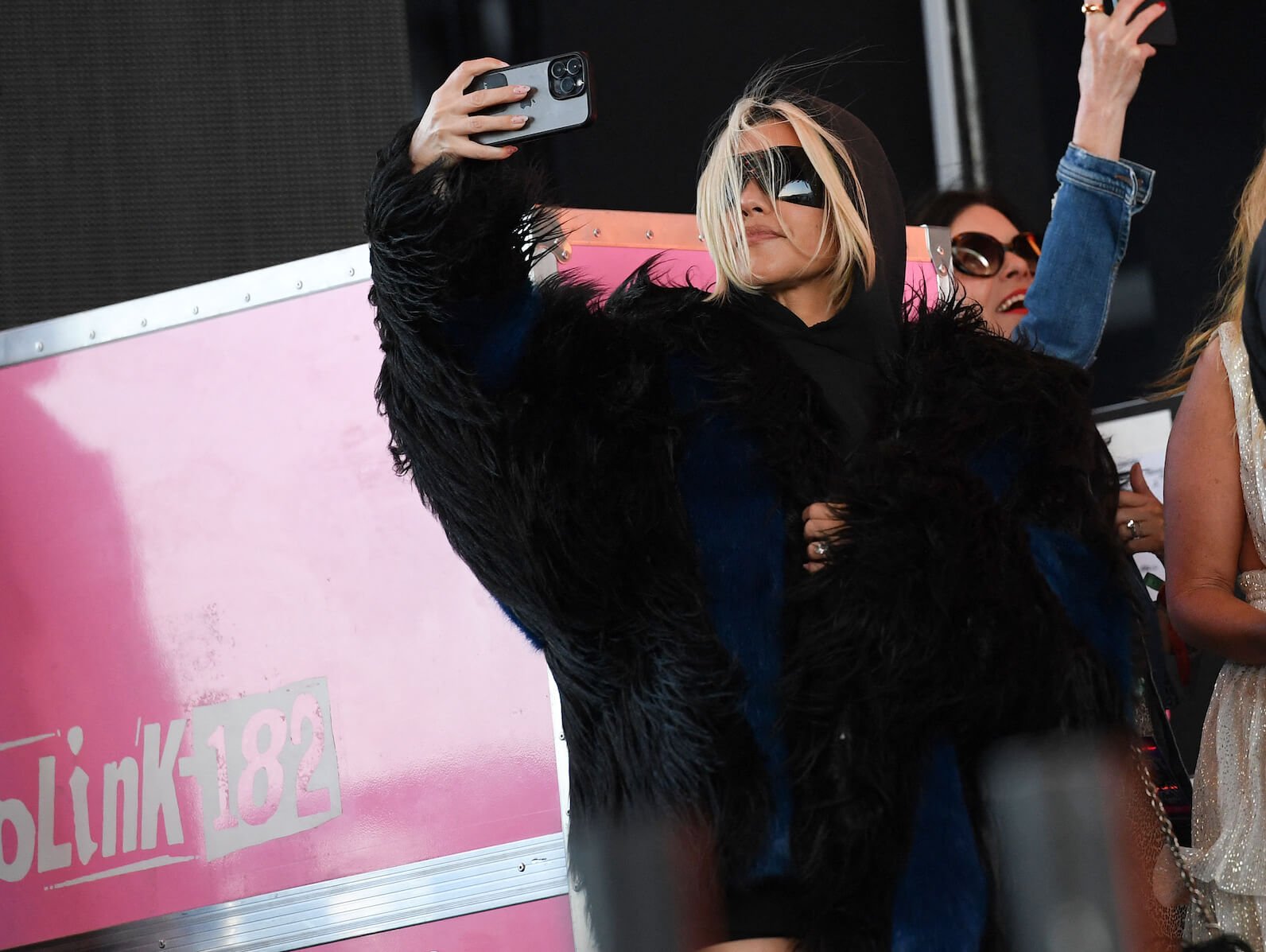 Kourtney Kardashian with blonde hair holding up her phone