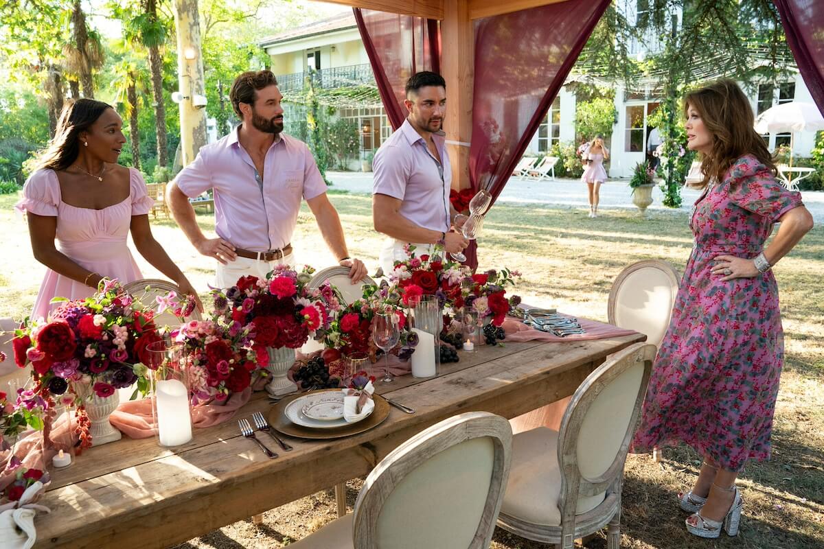 Lisa Vanderpump talks to a trio of staff members in pink shirts standing by an outdoor dining table in 'Vanderpump Villa'